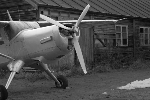 Black and white photo of a disused plane outside a rundown wooden hanger