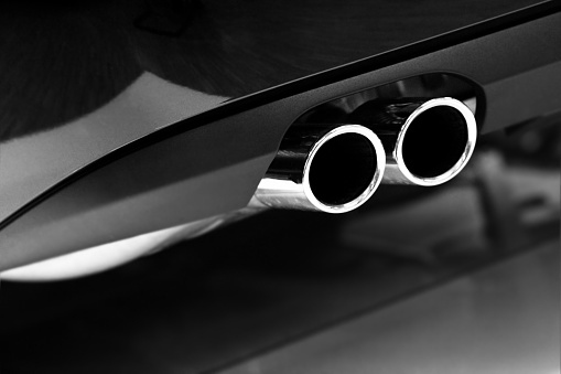 Close-up of metallic black luxury car exhaust pipe in chrome photographed in selective focus, low sharpening, shallow depth of field.  Rear view of vehicle on shiny black dealership floor.