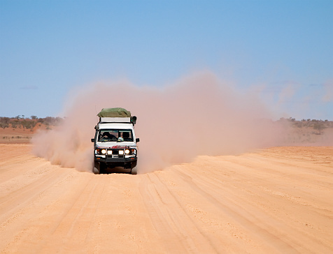 A heavily laden off road vehicle approaching on a dusty track.