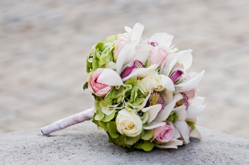 Close-up of pastel coloured Bridal Bouquet on stone block with soft focus background.