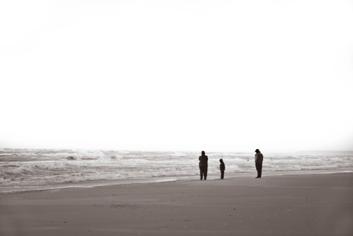 Family standing on the beach in stormy weather. Rough sea, blowing sand, burnt out skies. Løkken, Denmark.