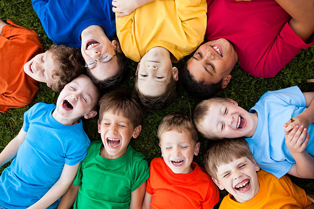 Happy Young Boys Laughing While Lying in a Circle Outside Color photo of a group of nine happy, young boys laughing while lying in the grass outside on a beautiful summer day. child laughing hysterically stock pictures, royalty-free photos & images