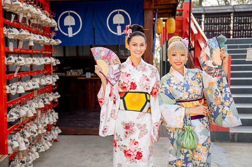 Portrait of Asian women wear japanese style dress with hold multicolor fan and stand in front of small shop and look happiness.