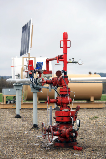 A natural gas wellhead with solar panel, storage tank, and plunger lift system. This well is located in Alberta, Canada. Vertical image. Valves and industrial equipment representative of the energy sector. Additional themes include fuel, power, methane, fossil fuel, gas, industrial equipment, industry, natural resource, and oil. 