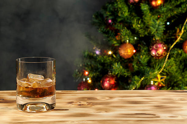 A glass of whiskey on a wooden table with a Christmas tree stock photo