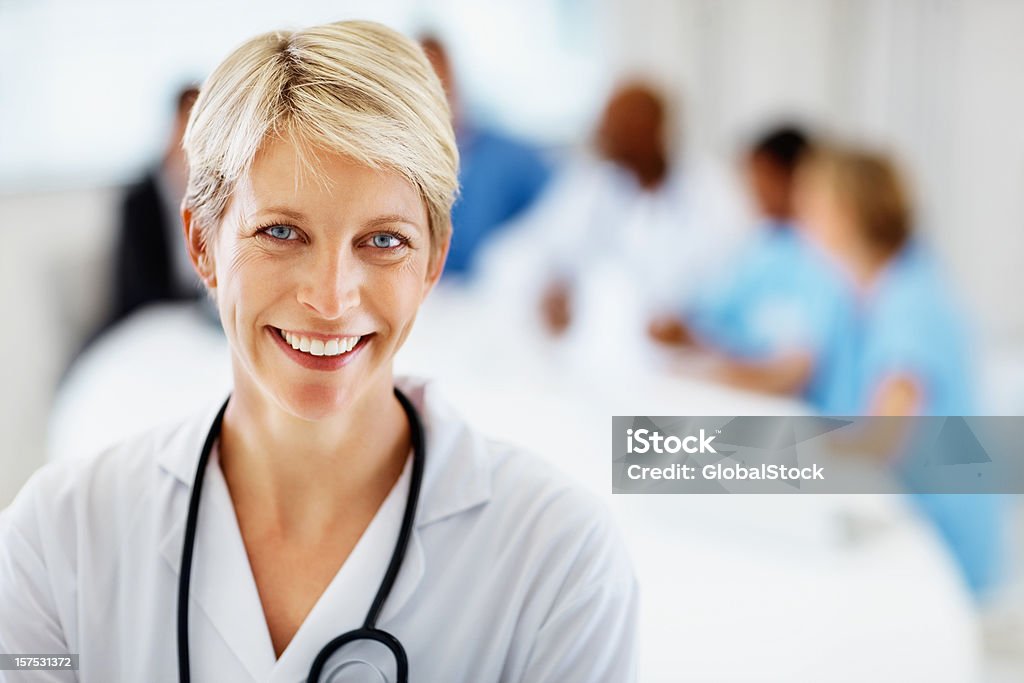 Mujer médico sonriente con colegas en la parte posterior - Foto de stock de Doctor libre de derechos