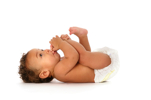 A biracial baby sitting sucking his toes isolated on white