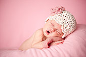 Sleeping Newborn Baby Girl Wearing a Crocheted Hat on Pink