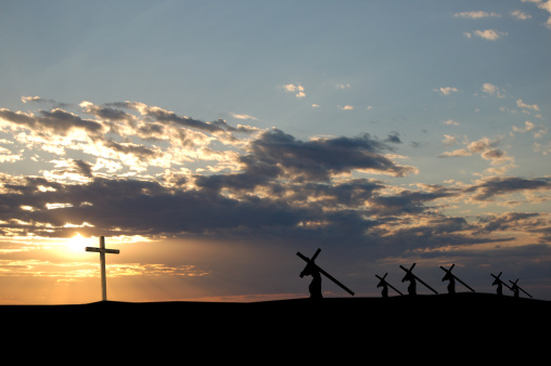 A group of figures carrying their crosses towards an illuminated cross.