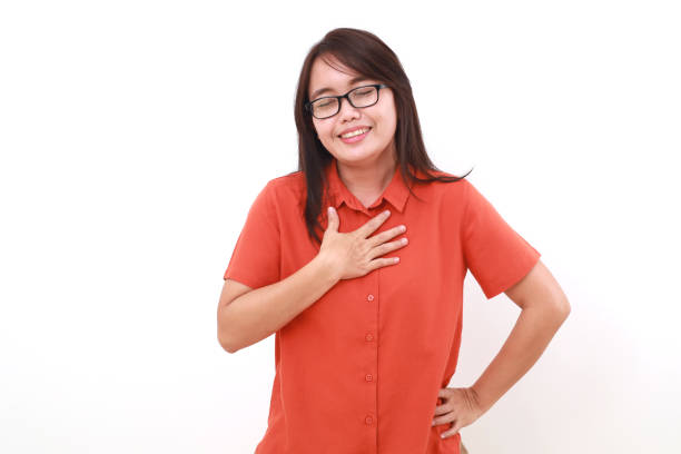 istock Relieved asian woman standing while holding her chest 1575329629