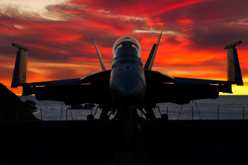 Silhouette of a military fighter jet aircraft entering the runway before take off in the sunset