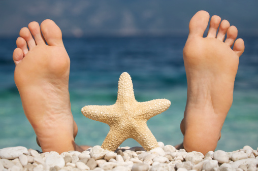 Starfish stands between two big feet sticking up from pebbled blue beach