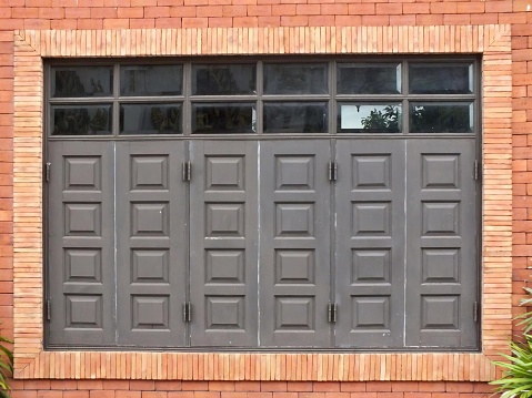a photography of a brick building with a large window and a cat sitting on a bench, there is a cat sitting on a bench in front of a garage door.
