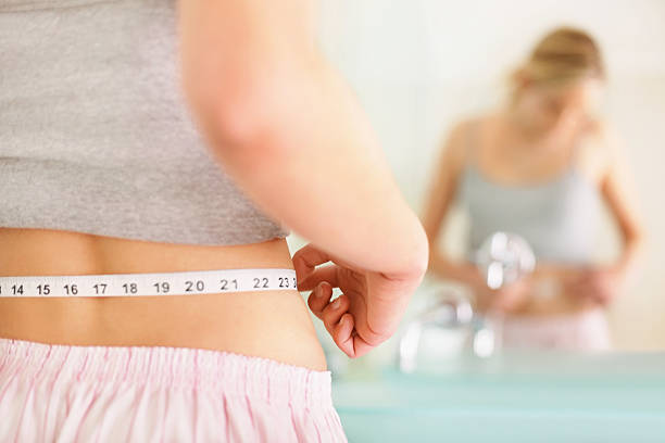 Rear view of woman measuring waist with mirror reflection Closeup of a young woman measuring her waist in the bathroom diets stock pictures, royalty-free photos & images