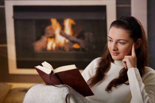 istock Woman reading a book near a fireplace 157534317