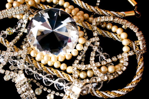 Large diamond with pearls, crystal and gold rope jewelry on black background.
