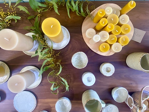 Horizontal flat lay of beeswax and soy handmade candles with ceramics and Australian native wattle leaves on timber domestic country table