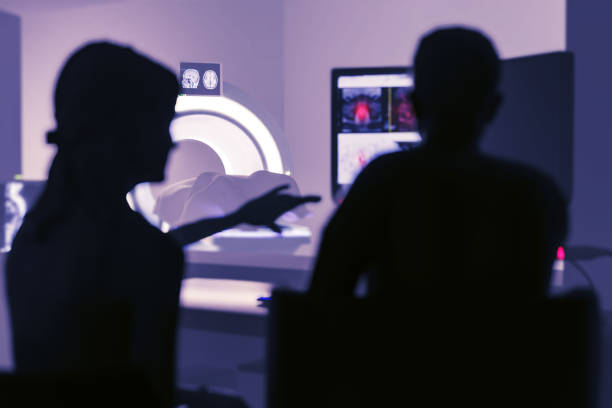 istock In Control Room Doctor and Radiologist Discuss Diagnosis while Watching Procedure and Monitors Showing Brain Scans Results, In the Background Patient Undergoes MRI or CT Scan Procedure.3D rendering . 1575401013