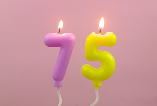 Burning air balloon shaped birthday candles on pink background, number 75