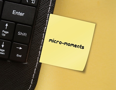 Note stick on keyboard with buzzword MICRO- MOMENTS,  small moments of consumers have throughout day before making a purchase decision - short precious times when brands get to interact with consumer