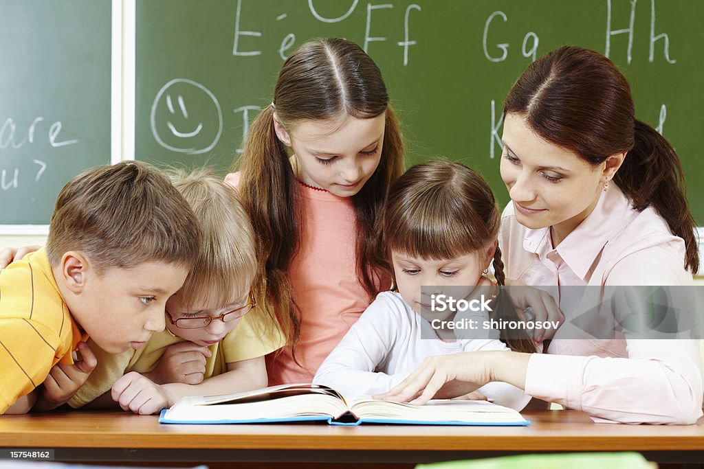 Reading Portrait of smart schoolchildren and their teacher reading book in classroom Adult Stock Photo