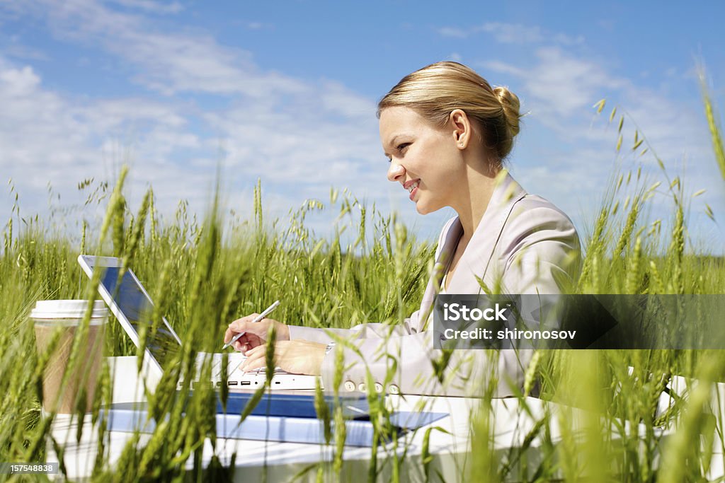 Businesswoman outdoor Image of businesswoman in suit sitting in green grass and typing Adult Stock Photo