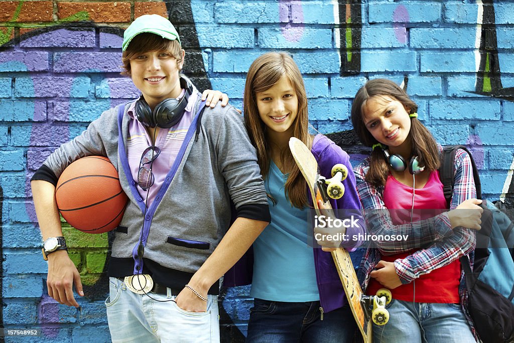 Youthful friends Row of happy teens by painted wall looking at camera Skateboard Stock Photo