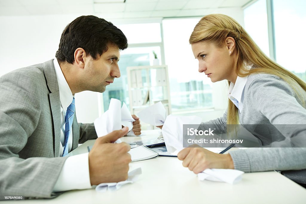 A disagreement between a man and a woman Profiles of angry employees with papers looking at each other strictly Adult Stock Photo