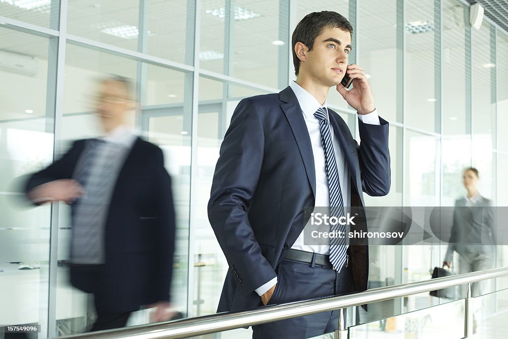 Calling Businessman standing by banisters and calling with walking people on background Blurred Motion Stock Photo