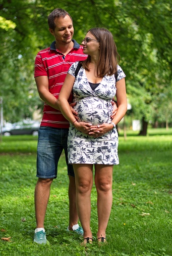 Pregnant couple touching woman's belly standing in park