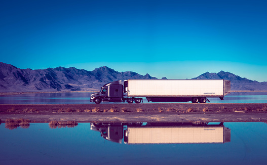 A mesmerizing scene as a semi truck drives through a salt lake, reflecting the stunning mountains in the background