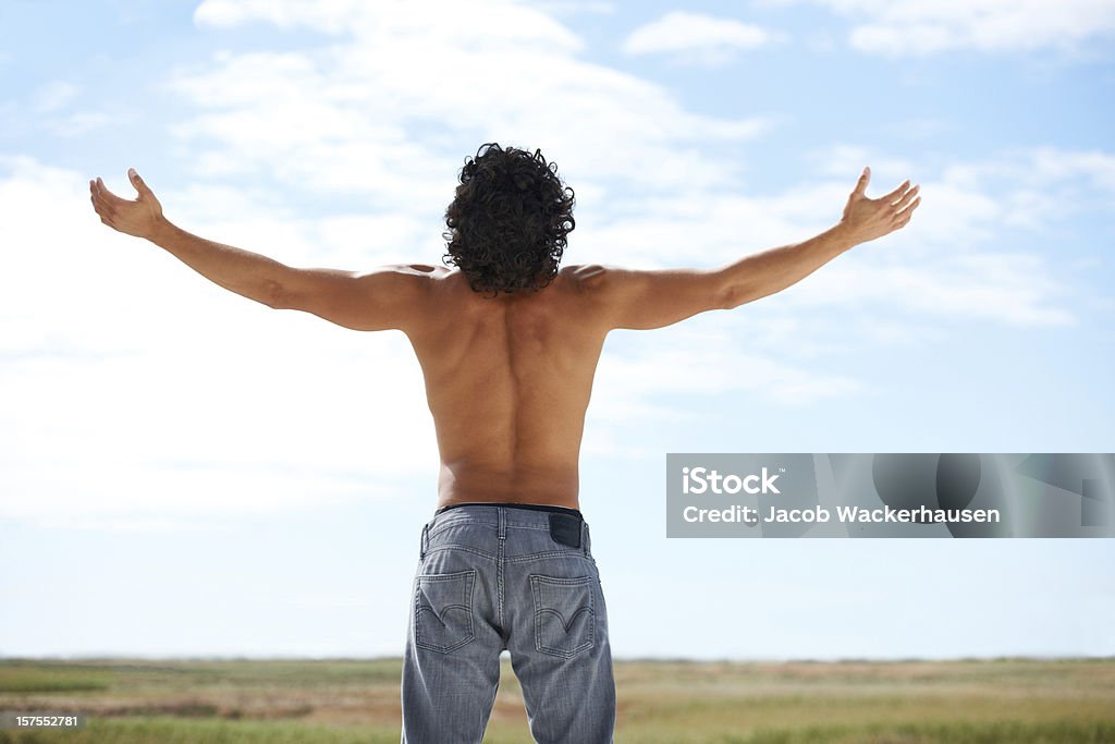 Letting go Rearview of young man wearing no shirt raising his arms to the sky Adult Stock Photo