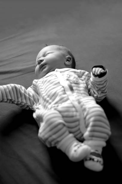 Extreme close-up (macro) monochromatic shot capturing the detail of a baby's small hand gently grasping a soft, textured blanket and a pacifier. The image conveys profound feelings of comfort, security, and the tenderness of early childhood. Ideal for parenting, healthcare, and lifestyle content focused on infants.