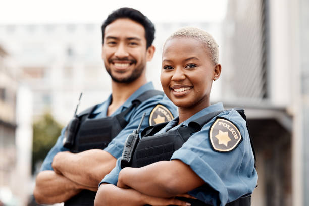 Happy police, team and arms crossed in confidence for city protection, law enforcement or crime. Portrait of man and woman officer standing ready for justice, security or teamwork in an urban town stock photo