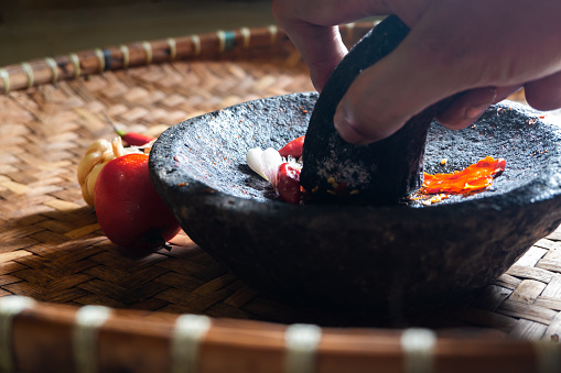 The figure of a hand grinding cayenne pepper and shallots with a mortar and pestle, or someone making chili sauce with a mortar and pestle made of stone.