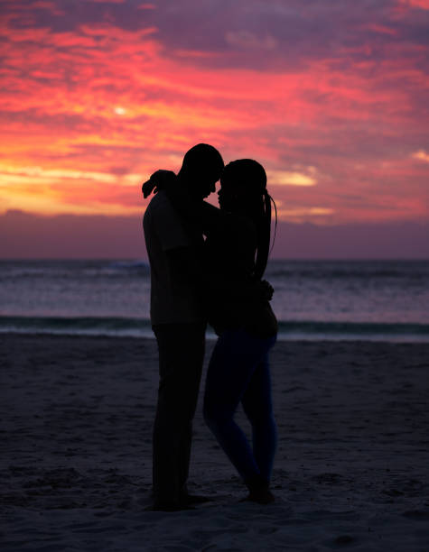 Couple, sunset and silhouette outdoor at the beach with love, care and commitment. Romantic man and woman hug or affectionate on vacation, holiday or nature travel adventure with sunrise sky on date Couple, sunset and silhouette outdoor at the beach with love, care and commitment. Romantic man and woman hug or affectionate on vacation, holiday or travel adventure with creative sky on date black couple sunset stock pictures, royalty-free photos & images