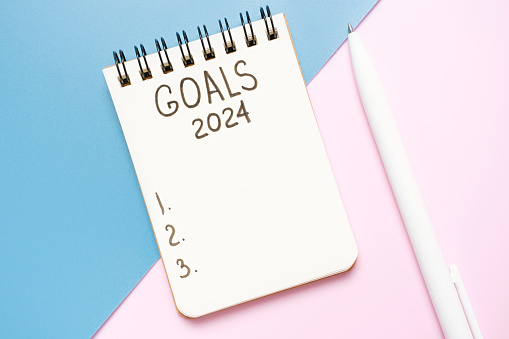The inscription goals 2024 on notepad on a pink and blue background, top view.