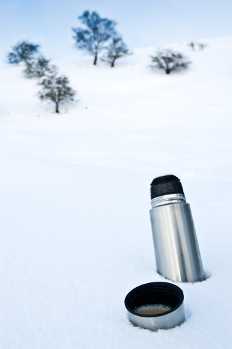 A royalty free stock photo of a flask of hot coffee sitting in the snow.-