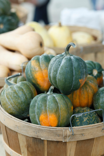 A basket overflowing with acorn squash at an outdoor farmers market.