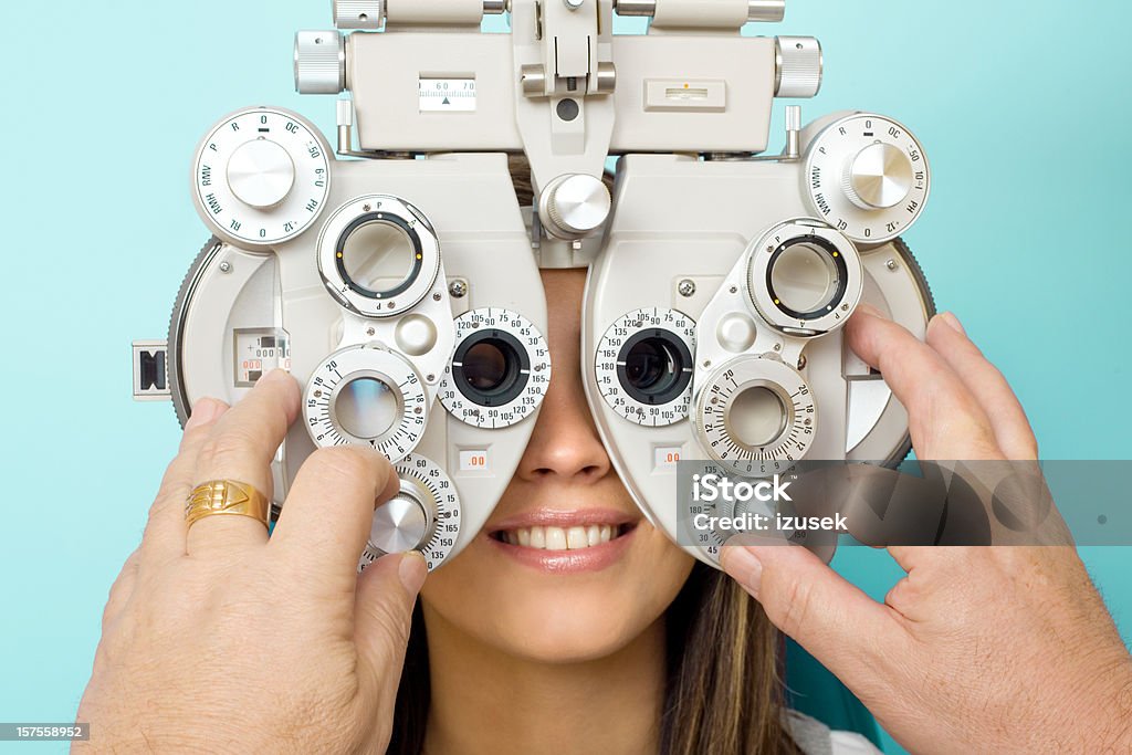 Optometrist Eye Exam Phoroptor Optometrist examines the eyes of a young woman patient with a phoroptor. Male hands adjusting dial on the phoroptor. Phoropter Stock Photo