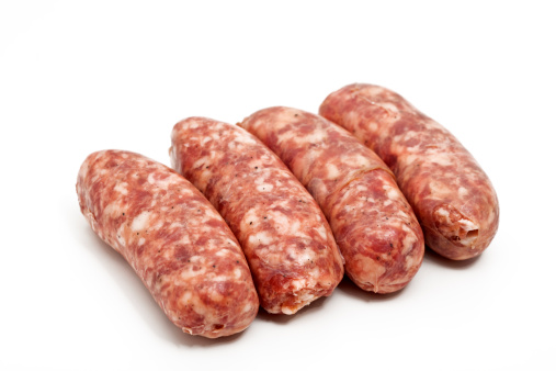 Raw sausages or bratwurst with spices and rosemary in a plate on black background. Close up. Food for grill or barbeque