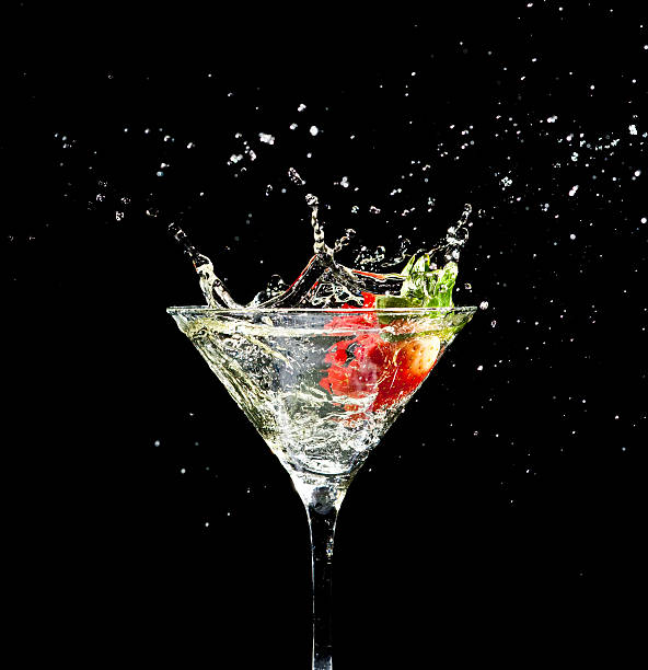 Strawberry splashing into glass of martini on a black backпround