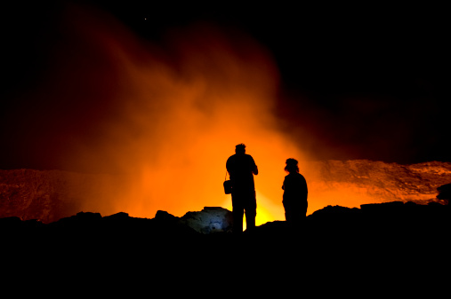 A couple of scientists standing on the crater rim of Erta Ale - one of the most active vulancoes in the world with an active, red glowing lava lake. 