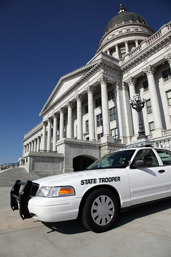 DSLR picture of a white state trooper police car in front of an office building. The sky is blue without a cloud. 