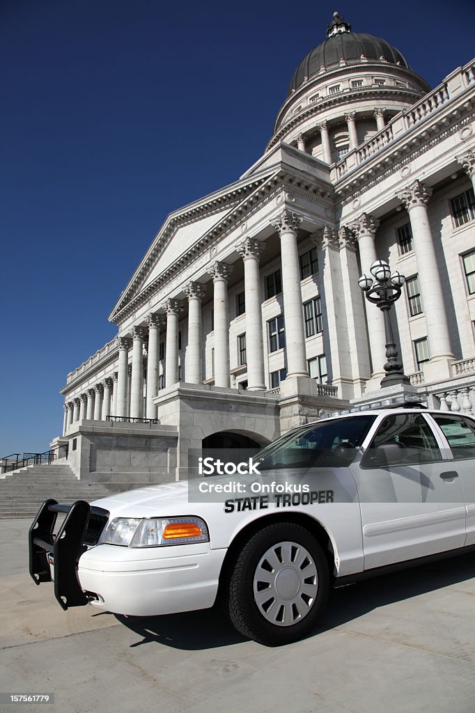 State Trooper Police Car in front of Office Capitol Building DSLR picture of a white state trooper police car in front of an office building. The sky is blue without a cloud.  Police Force Stock Photo