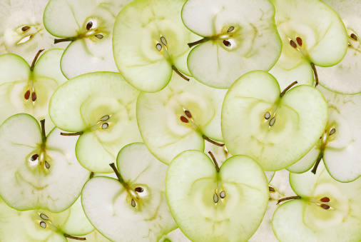 Background of thin slices of green apple. Slices are close to each other. High sharpness. Visible seeds, veins and stalk apple fruit.