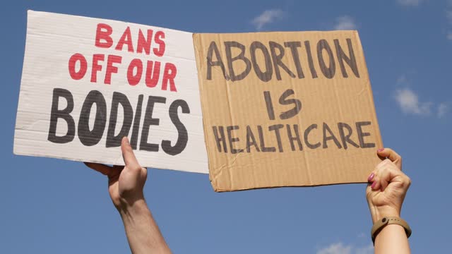 Protesters holding placard signs Abortion Is Healthcare and Bans Off Our Bodies.