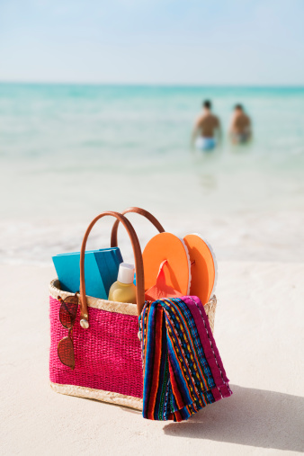 A young couple vacationing on their holiday in the Caribbean sea with their beach bag of suntan lotion, towel, book, sunglasses, flip flops and other personal accessories, equipment, and supplies for a tropical beach vacation get-away at Playa del Carmen, near Cancun, Riviera Maya, Mexico.