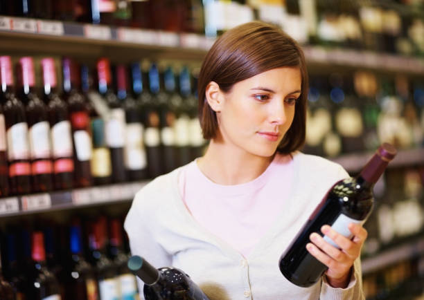 mujer joven en el supermercado frascos selección de vinos - vertical wine bottle variation rack fotografías e imágenes de stock