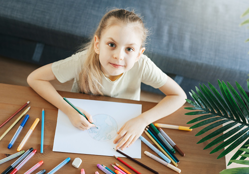 Child girl drawing with colorful pencils at home. Ecology concept, painting earth.